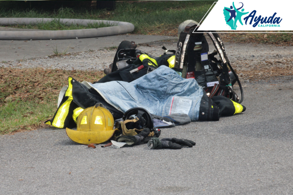 Equipo de protección de un bombero, incluyendo casco, guantes y chaqueta, tirado en el suelo junto a una manguera, simbolizando la gravedad del atropello y fuga sufrido mientras apagaba un incendio en Bakersfield. La imagen resalta la vulnerabilidad de los trabajadores de emergencia en carretera, como destaca Ayuda California.
